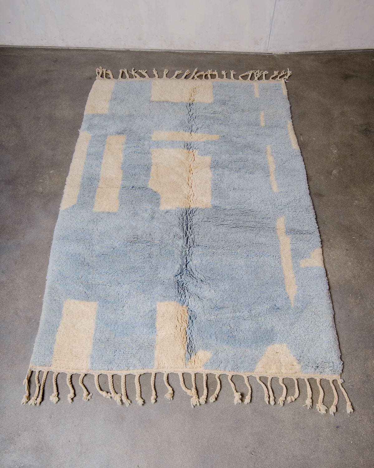 Berberlin Finest Beniourain Rug made of cream and baby blue wool laid flat on concrete floor.